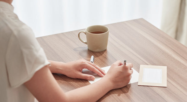 Person writing on a card at a desk with a coffee cup representing PR outreach and media pitching strategy